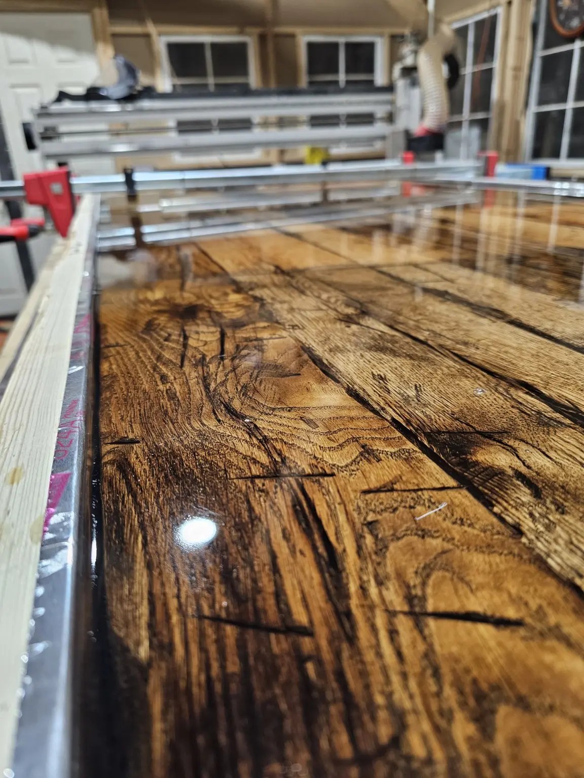 Glossy figured wood conference-table surface on the workshop bench, with dark grain running along its length.