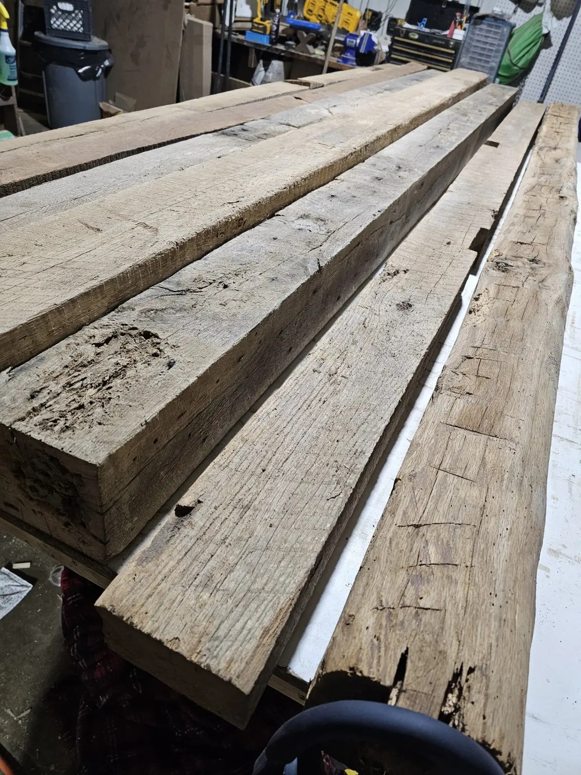Long rough wood beams laid side by side on the workshop bench before the conference-table build.