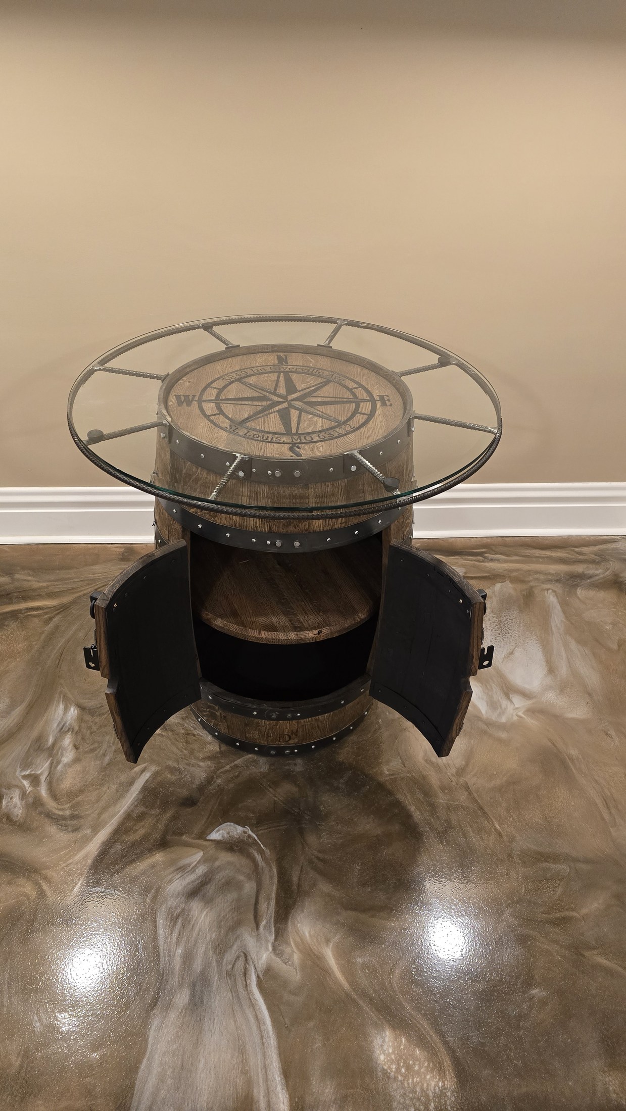 Barrel cabinet with curved doors open below an engraved top, rebar surround and glass surface.