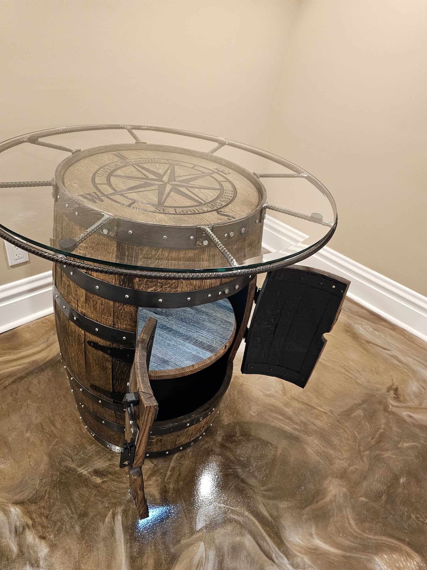 Engraved compass-style barrel top beneath a circular rebar frame and glass surface beside the shelving room.