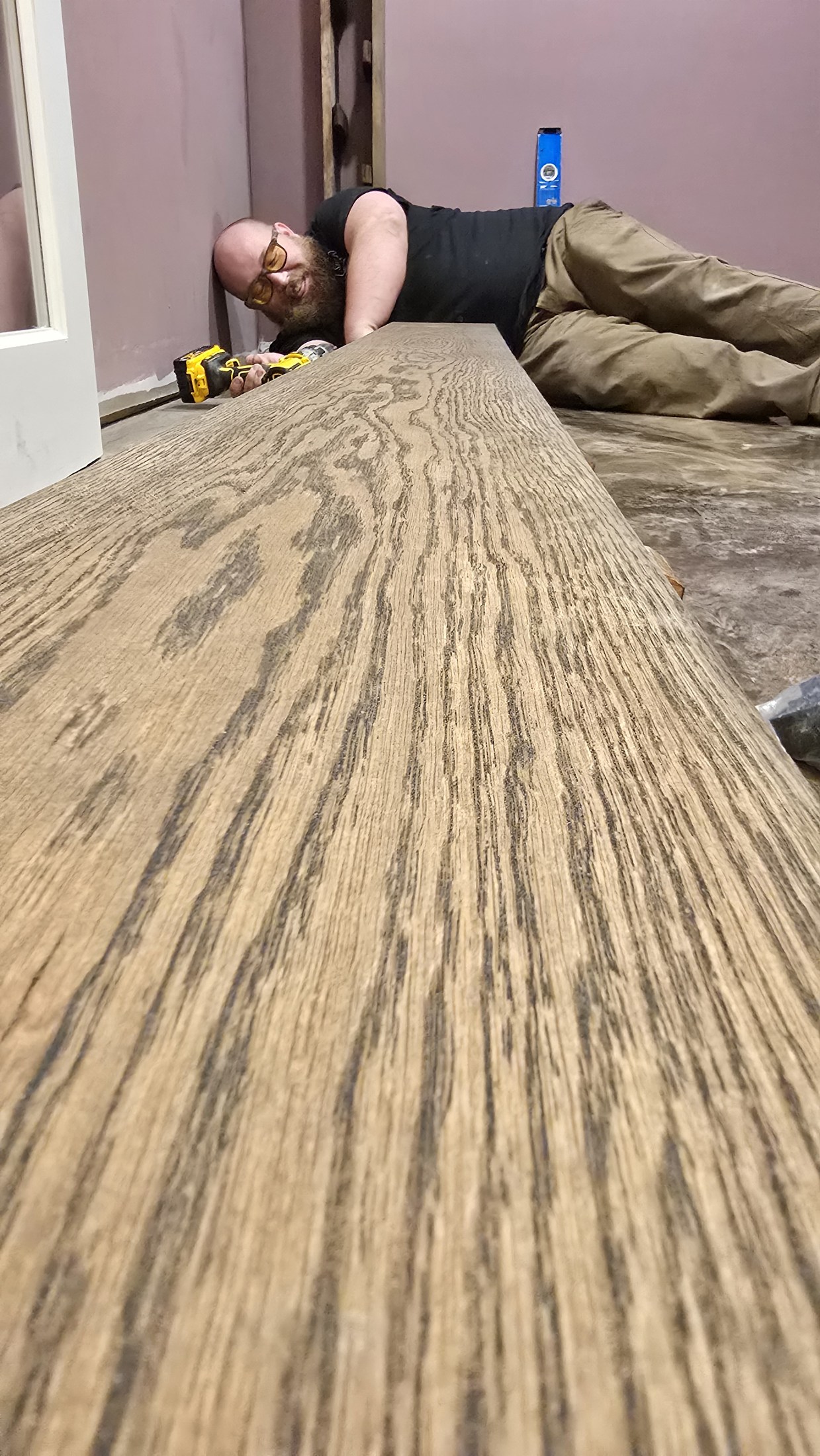 Ryan works at floor level beside a broad wood shelf and tools during installation.